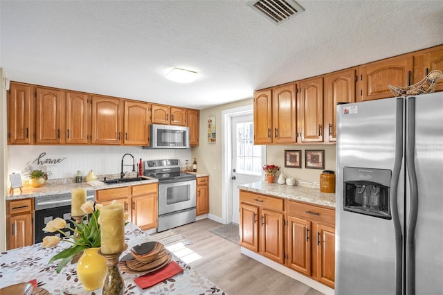 kitchen featuring light stone counters, light wood-type flooring, sink, and appliances with stainless steel finishes