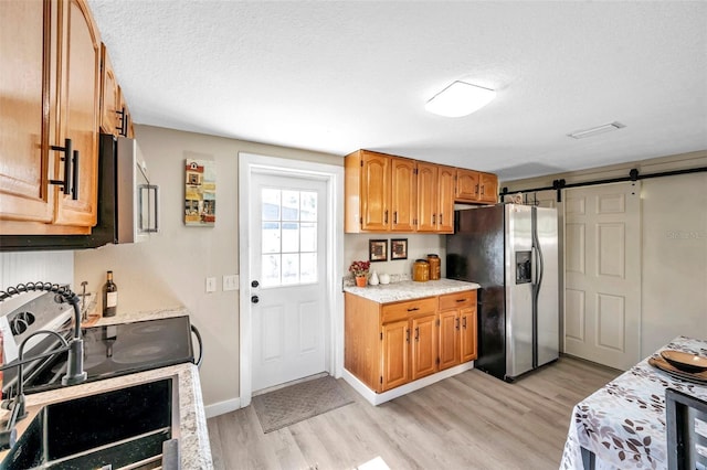 kitchen with a barn door, stainless steel appliances, a textured ceiling, and light wood-type flooring