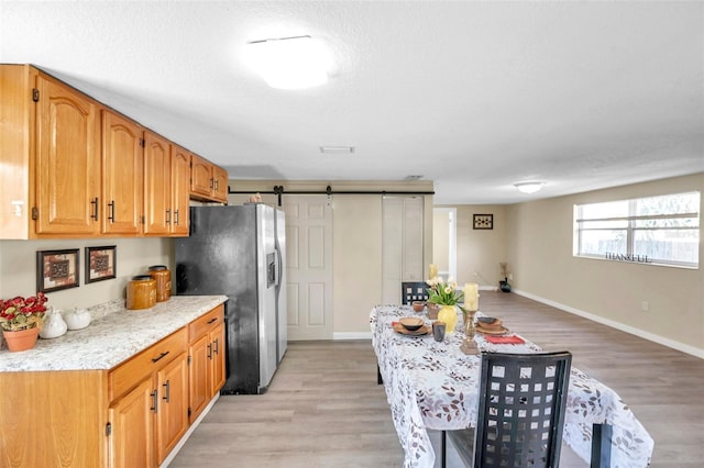 kitchen with a textured ceiling, a barn door, stainless steel refrigerator with ice dispenser, and light wood-type flooring