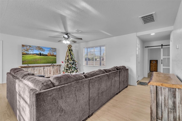 living room featuring a textured ceiling, a barn door, light hardwood / wood-style flooring, and ceiling fan