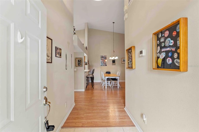 hallway with hardwood / wood-style flooring, high vaulted ceiling, and a notable chandelier