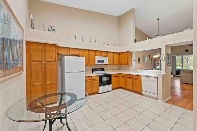 kitchen with sink, a towering ceiling, white appliances, light tile patterned floors, and ceiling fan with notable chandelier