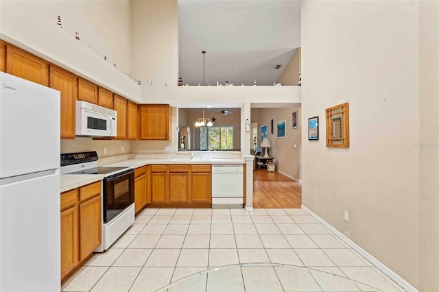 kitchen with a towering ceiling, white appliances, light tile patterned floors, pendant lighting, and a notable chandelier