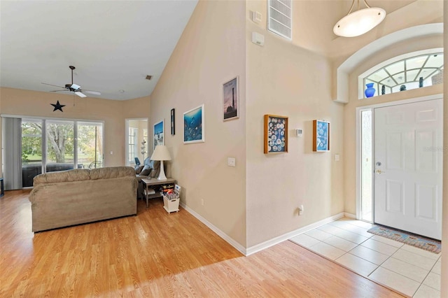 foyer entrance featuring a towering ceiling, light wood-type flooring, and ceiling fan