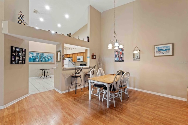 dining room with light hardwood / wood-style floors, a towering ceiling, and a chandelier