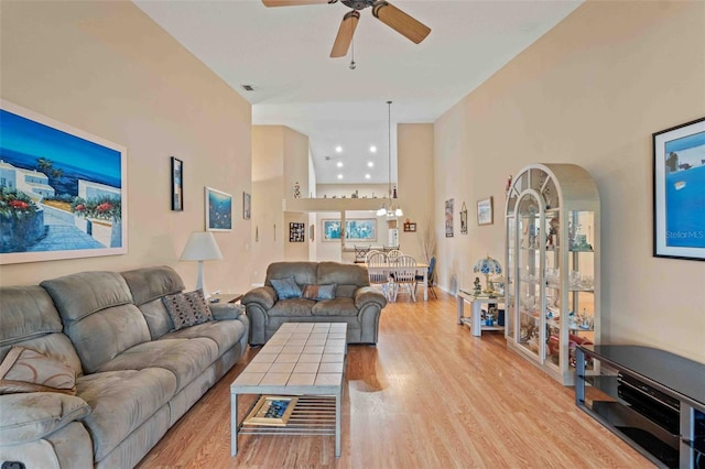 living room with ceiling fan, light wood-type flooring, and a high ceiling