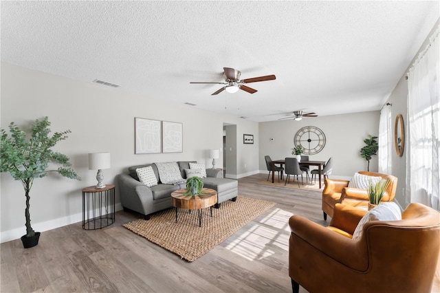 living room featuring a textured ceiling, light wood-type flooring, and ceiling fan