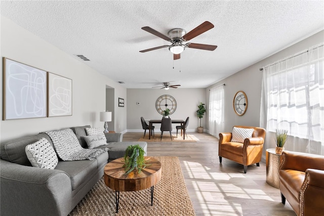 living room with a textured ceiling, light hardwood / wood-style floors, and ceiling fan