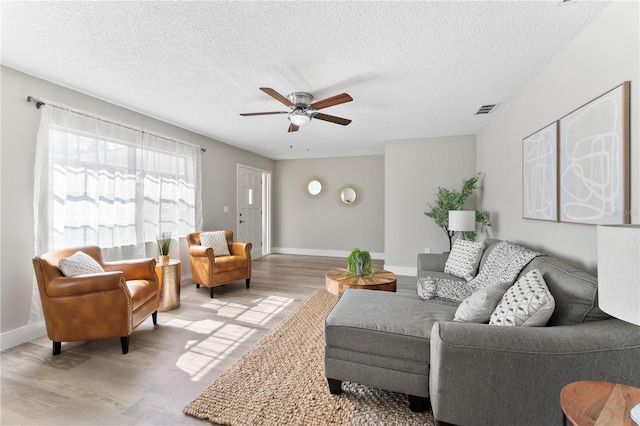 living room featuring ceiling fan, light hardwood / wood-style flooring, and a textured ceiling