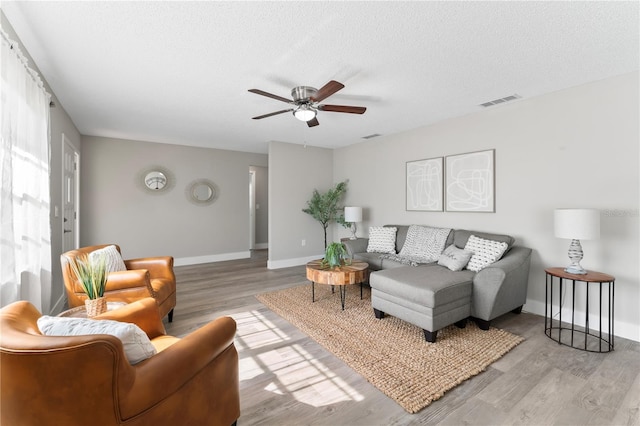 living room with a textured ceiling, light wood-type flooring, and ceiling fan