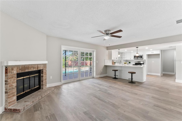 unfurnished living room with a fireplace, a textured ceiling, light hardwood / wood-style flooring, and ceiling fan