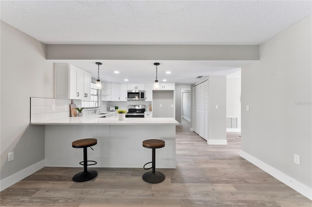 kitchen featuring white cabinets, appliances with stainless steel finishes, decorative light fixtures, light hardwood / wood-style floors, and kitchen peninsula