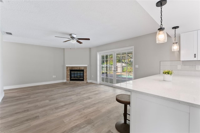 living room with french doors, a brick fireplace, a textured ceiling, ceiling fan, and light hardwood / wood-style floors