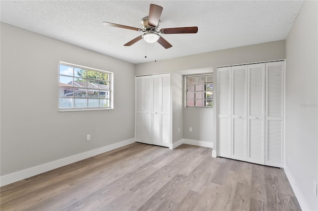 unfurnished bedroom with light wood-type flooring, a textured ceiling, ceiling fan, and multiple closets