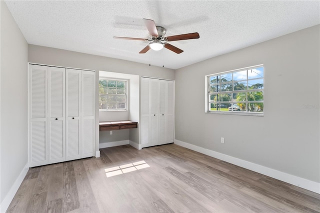 unfurnished bedroom with a textured ceiling, light hardwood / wood-style floors, ceiling fan, and multiple closets