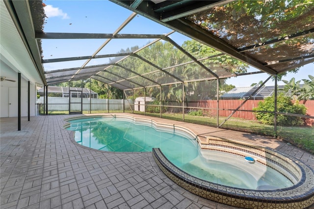 view of swimming pool with glass enclosure, a storage unit, and a patio