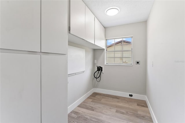 laundry room with electric dryer hookup, cabinets, a textured ceiling, and light hardwood / wood-style flooring