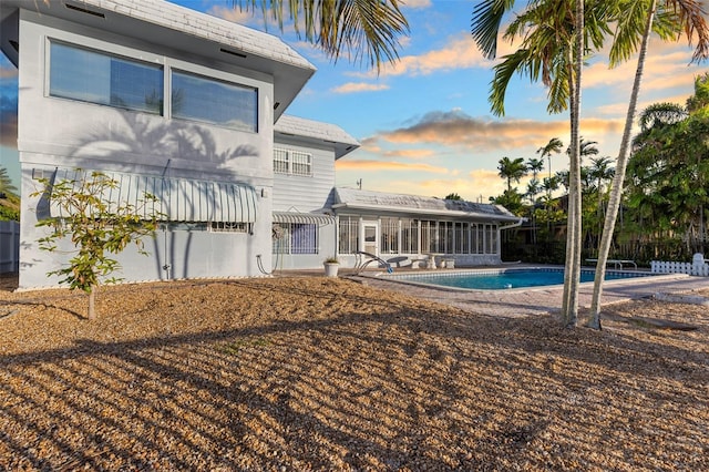 back house at dusk with a patio, a fenced in pool, and a sunroom