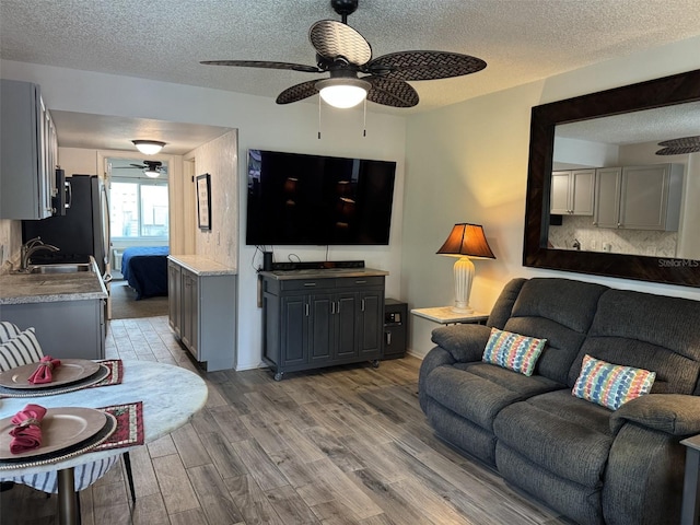 living room with ceiling fan, sink, a textured ceiling, and hardwood / wood-style flooring