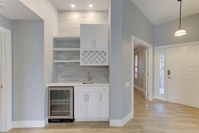 bar featuring light wood-type flooring, beverage cooler, sink, decorative light fixtures, and white cabinetry