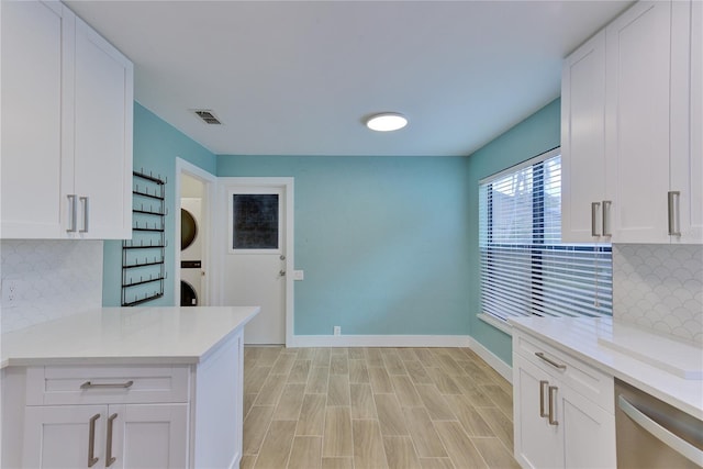 kitchen featuring white cabinets, decorative backsplash, and stacked washer / dryer