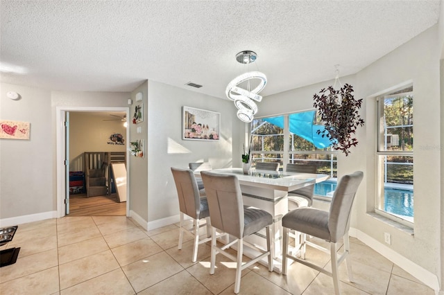 dining room with a textured ceiling, plenty of natural light, light tile patterned floors, and ceiling fan with notable chandelier