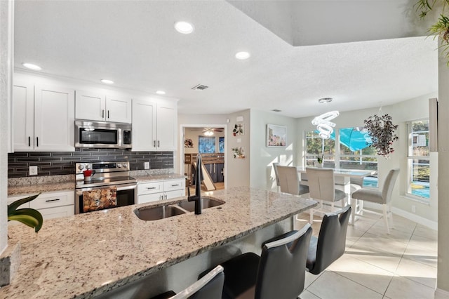 kitchen featuring white cabinets, sink, light stone countertops, light tile patterned floors, and appliances with stainless steel finishes