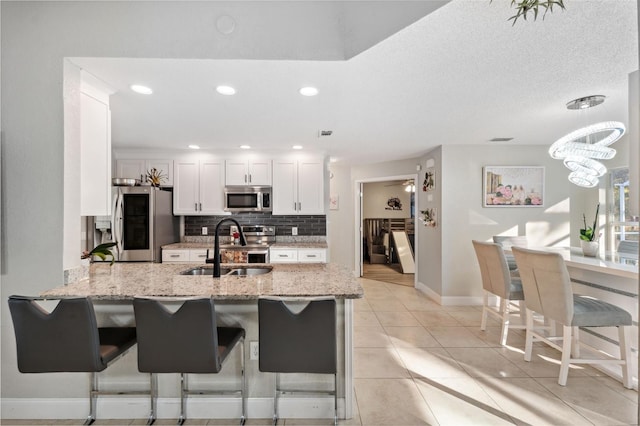 kitchen with kitchen peninsula, stainless steel appliances, sink, white cabinets, and light tile patterned flooring