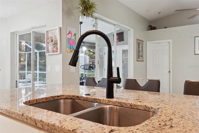 kitchen featuring ceiling fan, light stone counters, lofted ceiling, and sink