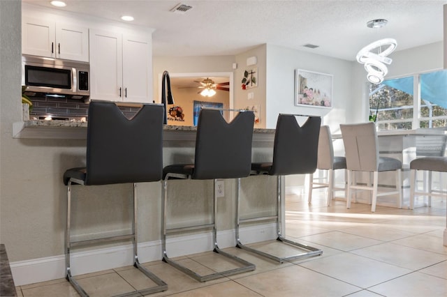 kitchen with decorative backsplash, stone counters, white cabinets, and ceiling fan with notable chandelier