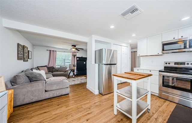 kitchen featuring visible vents, light wood-style flooring, stainless steel appliances, white cabinetry, and open floor plan