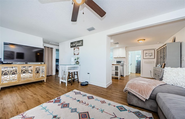 living area featuring visible vents, a ceiling fan, baseboards, and wood finished floors