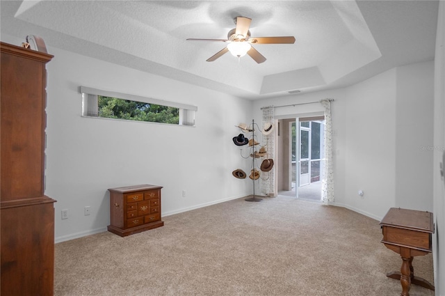 interior space featuring ceiling fan, a raised ceiling, light colored carpet, and a textured ceiling