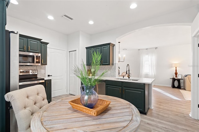 kitchen with sink, appliances with stainless steel finishes, tasteful backsplash, light hardwood / wood-style floors, and kitchen peninsula