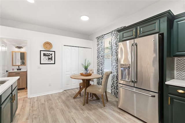 kitchen featuring backsplash, light hardwood / wood-style floors, green cabinets, and stainless steel refrigerator with ice dispenser