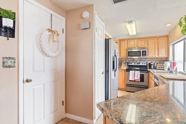 kitchen with decorative backsplash, kitchen peninsula, a textured ceiling, stainless steel appliances, and stone counters