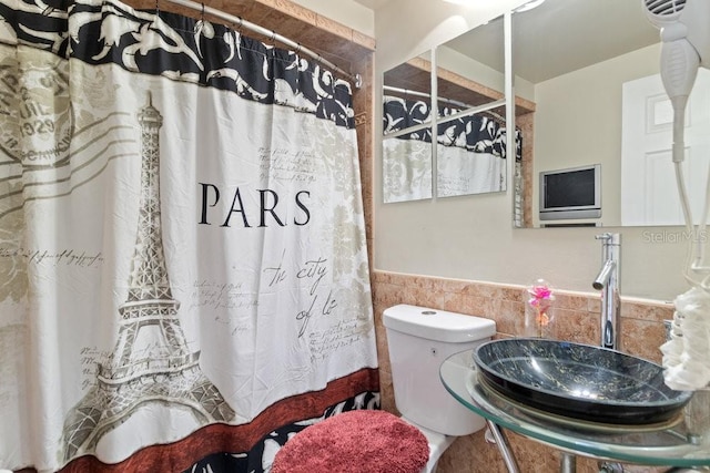 bathroom featuring toilet, tile walls, and sink