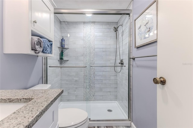 bathroom featuring a shower with door, vanity, and toilet