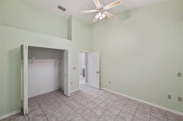 unfurnished bedroom with light tile patterned floors, a towering ceiling, a closet, and ceiling fan