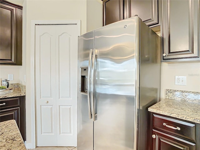 kitchen featuring dark brown cabinetry, light stone countertops, light tile patterned floors, and stainless steel refrigerator with ice dispenser