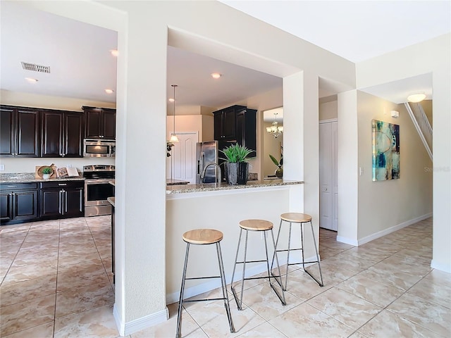 kitchen with light stone countertops, kitchen peninsula, a breakfast bar, stainless steel appliances, and a chandelier