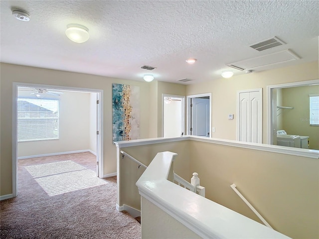 hallway with light carpet, a textured ceiling, and washing machine and dryer