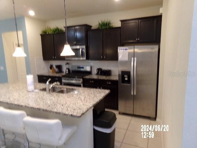 kitchen featuring light stone countertops, hanging light fixtures, stainless steel appliances, a breakfast bar area, and a kitchen island with sink