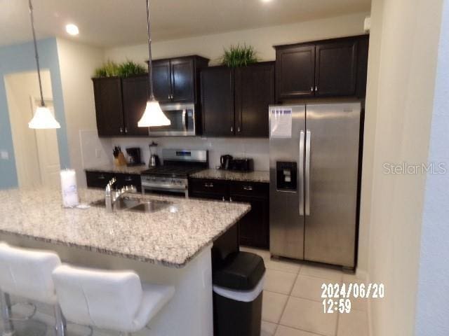 5537 Misty Oak Cir, Davenport, FL 33837 - kitchen with appliances with stainless steel finishes, light stone counters, dark brown cabinets, light tile patterned floors, and hanging light fixtures