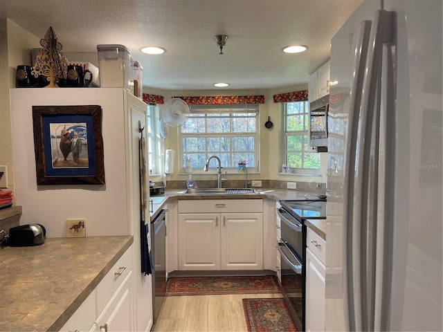 kitchen with appliances with stainless steel finishes, a textured ceiling, sink, light hardwood / wood-style flooring, and white cabinetry