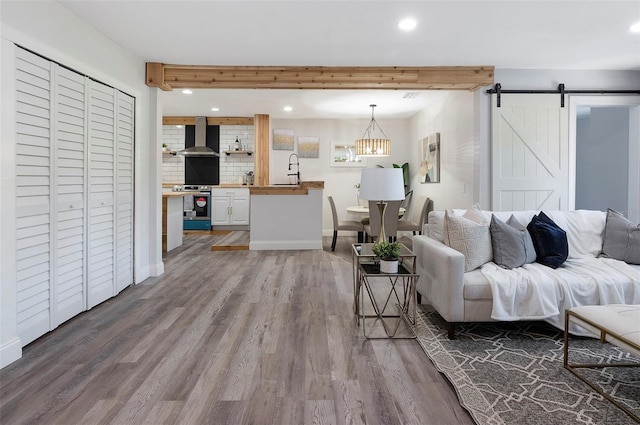 living room featuring beam ceiling, a barn door, light hardwood / wood-style floors, and sink