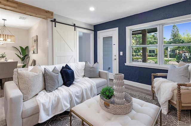 living room with hardwood / wood-style flooring, a barn door, beamed ceiling, and an inviting chandelier