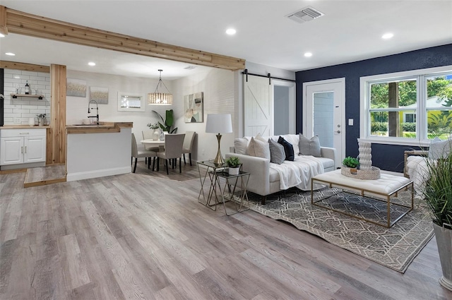 living room with beam ceiling, a barn door, light hardwood / wood-style floors, and sink