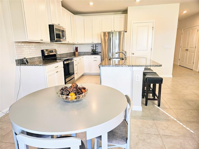 kitchen with dark stone counters, light tile patterned floors, decorative backsplash, stainless steel appliances, and a kitchen island with sink