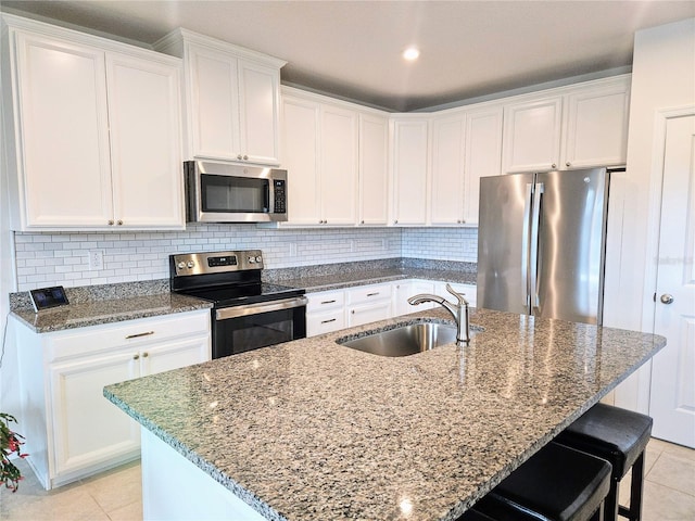 kitchen with a sink, stainless steel appliances, light tile patterned flooring, white cabinets, and decorative backsplash